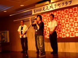 4人で壇上に上がりスピーチを行う男性の写真