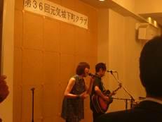 壇上でギター演奏の男性と歌を披露する女性の様子の写真
