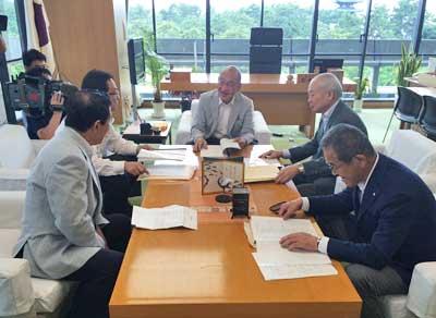 明るい茶色の机を囲み、書類に目を通している男性らの写真