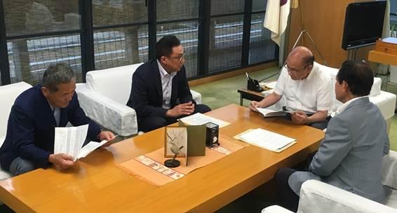 茶色い机を囲って4人の男性が打ち合わせをしている写真