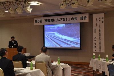 第5回「奈良県にリニアを!」の会」と書かれた横断幕とプロジェクターの映像を使って講演している写真