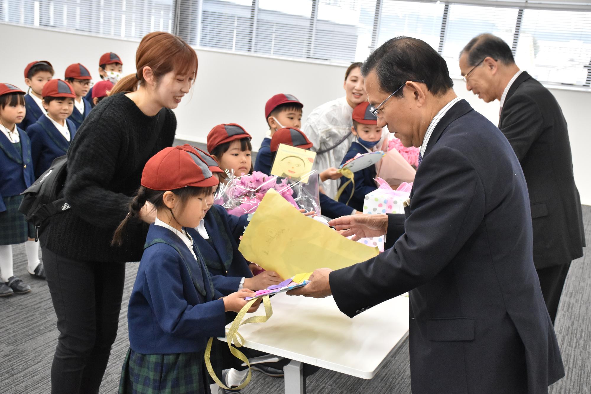 カトリック幼稚園の園児から市長、教育長へ感謝の花束と手作りのメダルが手渡されている様子