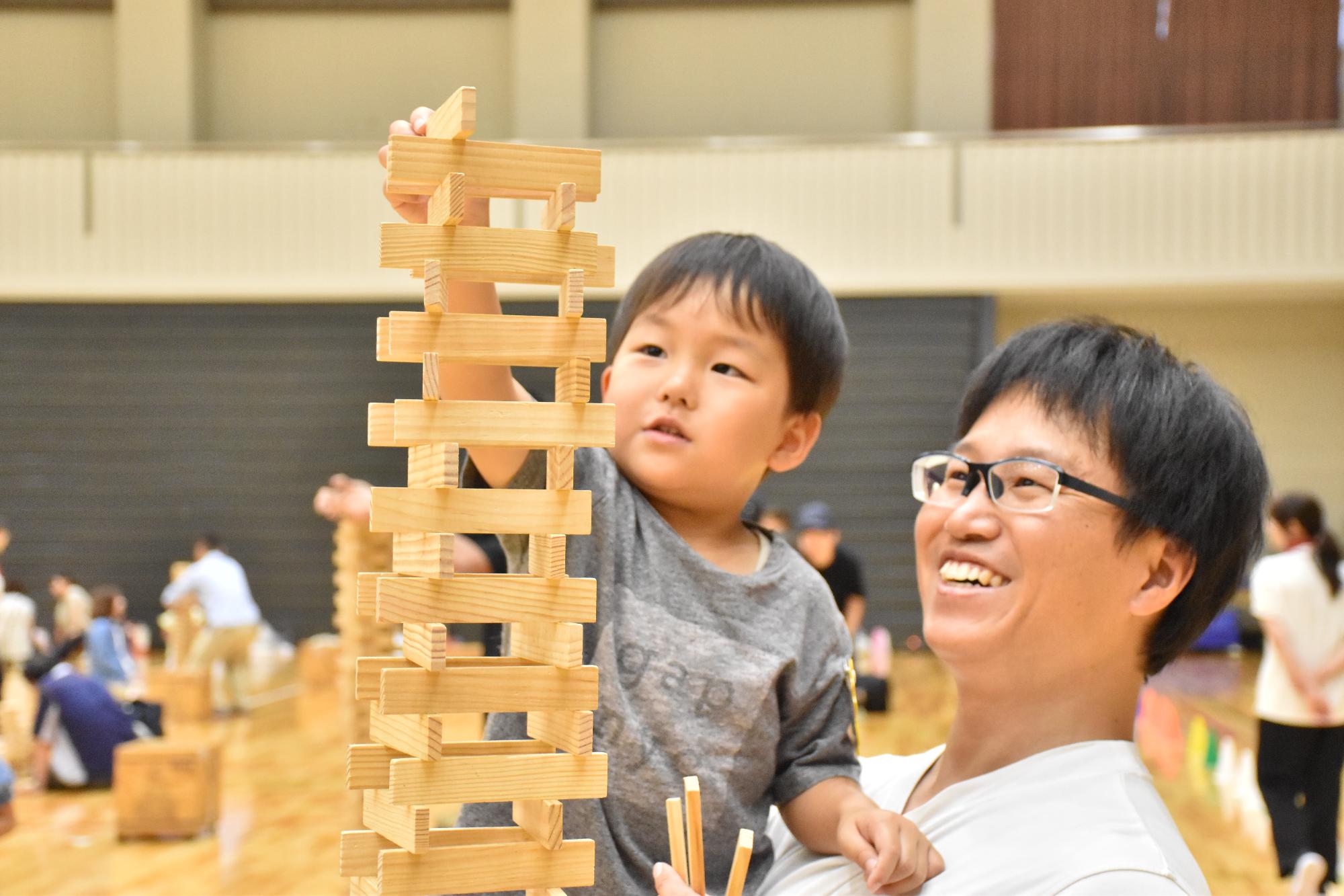 第23回カプラ親子フェスタで抱っこされた子どもがカプラを積み上げる