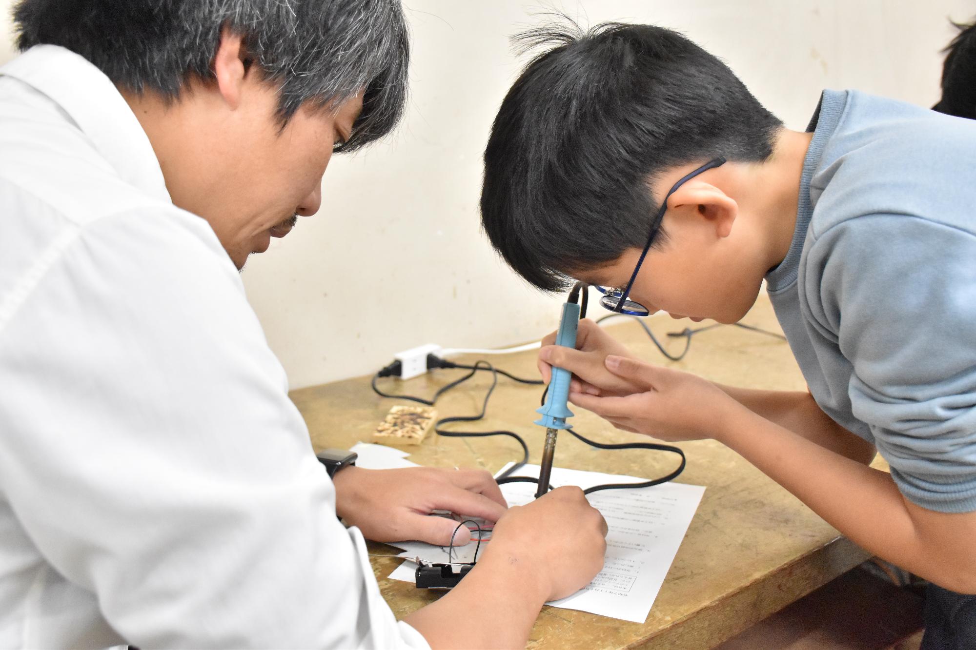 科学教室で慎重にはんだごてを扱う受講生とサポートする先生