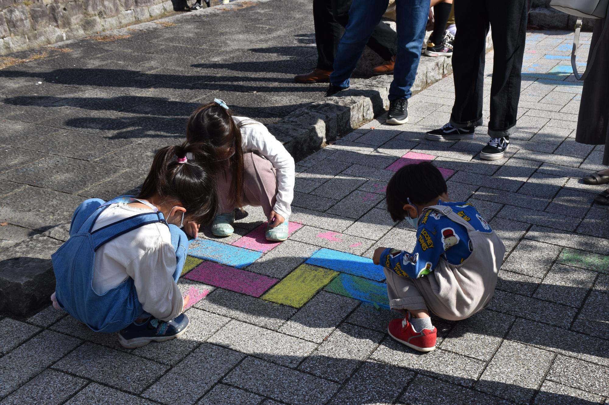 石畳をチョークで塗る3人の子どもたち