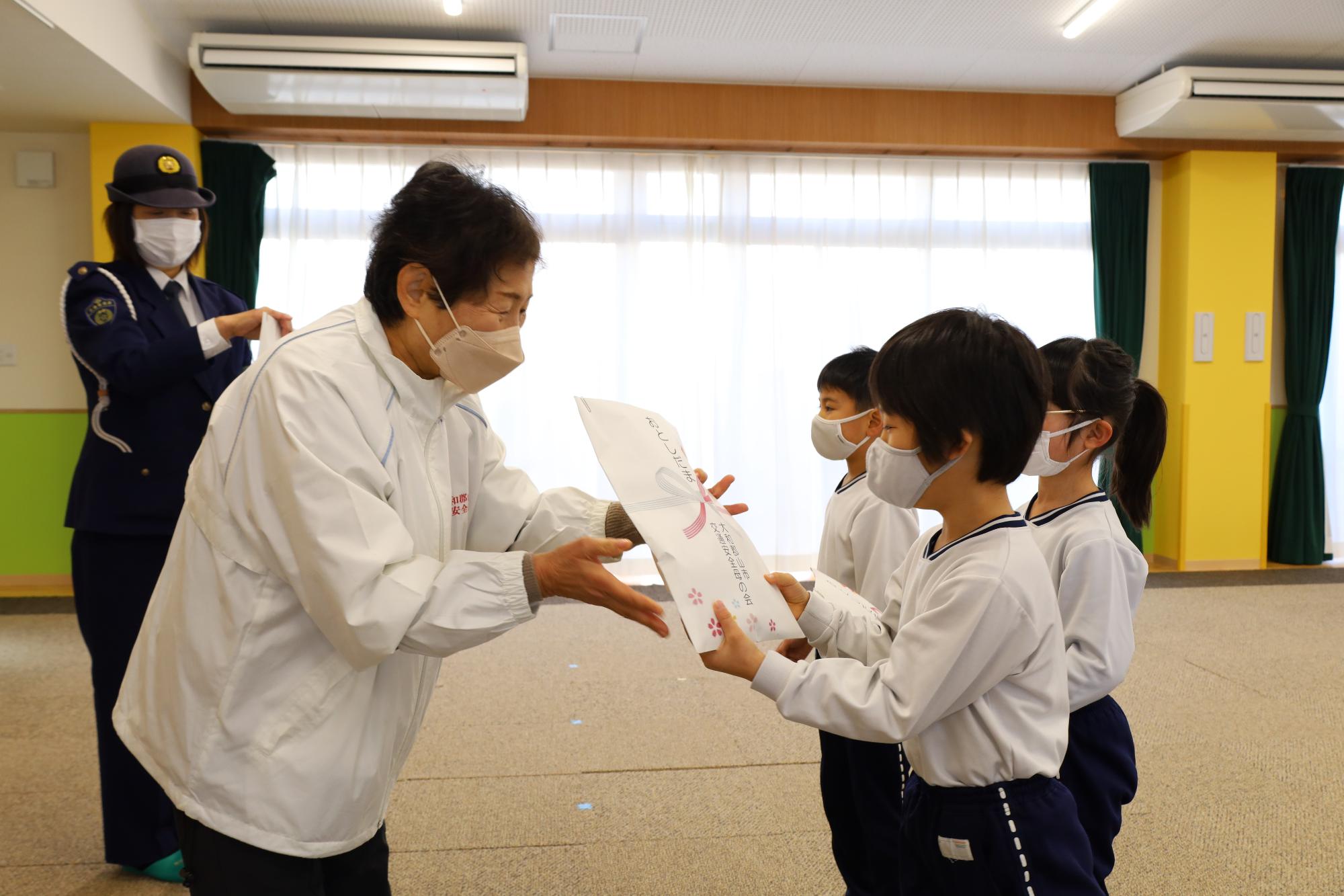 3人の園児にお年玉の反射板を渡す交通安全母の会の女性