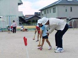 年配者にグラウンドゴルフを教わっている保育園児の写真