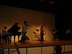 舞台の上で、ピアノとバイオリンを演奏する男女5人の写真