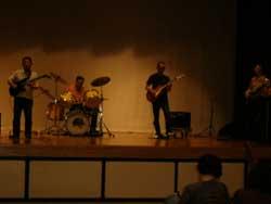 舞台の上で、ギターとドラムの演奏をする4人の写真