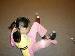 倒れているペットボトルを足を使って立てて遊んでいる女児の写真