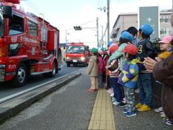 道路を走る消防車を並んでみている子供たちの写真