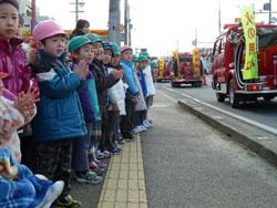 道路を走る消防車拍手をしながらみている子供たちの写真