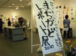 手書きの「まちかどレポート展2010」の立て看板と展示場内の写真