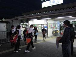 夜人が行き交う駅前で募金活動をする人々の写真