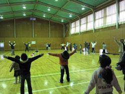 体育館でラジオ体操をする子どもたちが胸を開く姿勢をしている写真