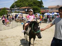 帽子をかぶった子供が、大人に手綱を引かれた馬に乗ってポーズをとっている写真