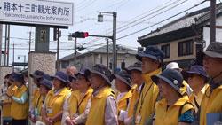 お揃いの黄色いベストと紺の帽子をかぶっている式典を見守る観光ボランティアガイドクラブの人たちの写真