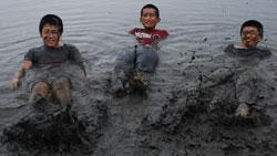 泥田の中を泥まみれになって横たわっている3人の子供の写真