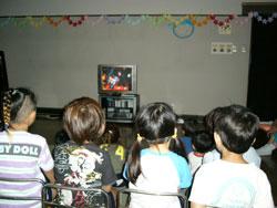 暗くした教室でビデオを見る園児たちの写真