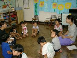 床に円になって座る園児と先生の写真