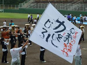 野球場の吹奏楽の中、大きな旗を広げるスタッフの方の写真