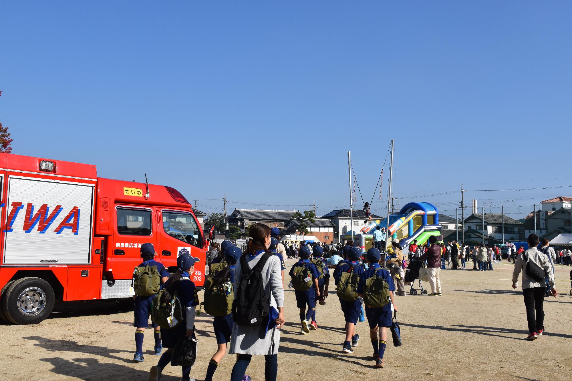 消防車やイベント用遊具が並び、ボーイスカウトの子ども達が集まって来ている親子まつり会場