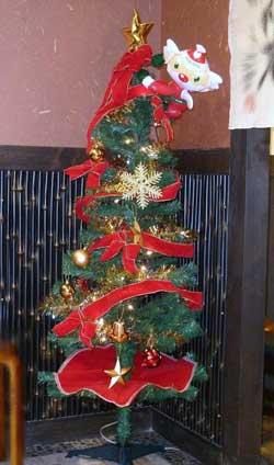 赤いリボンが巻いてあり、雪結晶とサンタのモチーフが飾られたクリスマスツリーの写真。