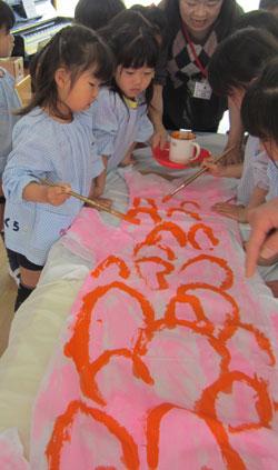 子供たちが筆を使って赤い鱗の模様を書いている写真