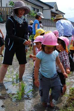 水田に足を踏み込んでいる園児たちと園長先生の写真