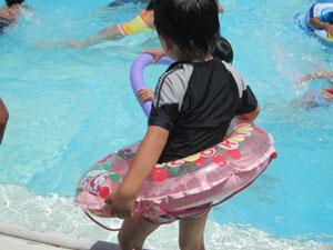 子供向けプールで遊ぶ、ピンクの浮き輪をつけた女の子の写真
