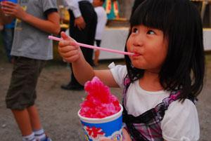 赤いシロップをかけたかき氷を美味しそうに食べている女の子の写真