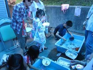 青い水槽で金魚すくいをしている子どもたちの写真