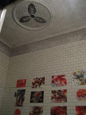 お風呂のタイルの壁に何枚か写真が並べられており、天井には、三枚の葉が家紋のような雰囲気で描かれている写真