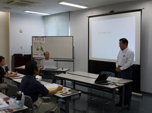 スクリーンの前に立つ上田市長とホワイトボードの前に座る男性と参加者の写真