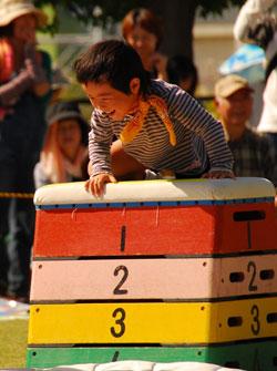オレンジのスカーフをした男の子が跳び箱の上にお腹を下にして乗っている写真