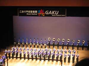 舞台上に整列し紫色のユニフォームを着た天理教校学園高校のマーチングバンドの演奏の様子の写真