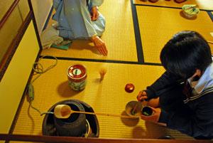男の子が、茶道のお茶を立てる道具の前で、器に葉を入れている上部からの写真