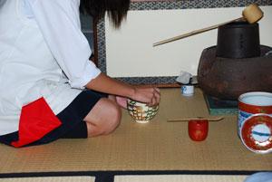 茶道茶道の道具の前で、女の子がお茶碗を右手で触ってお辞儀をしている様子。