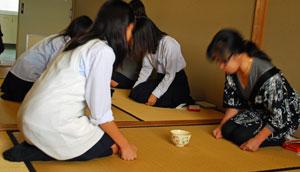 4人の女の子が畳の上で正座し向き合って、お茶碗を前にお辞儀をしている様子。
