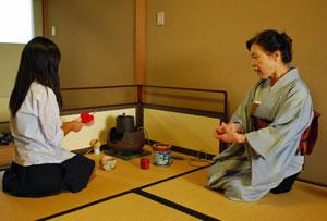 左に女の子がお茶を立てる道具の前で正座で座っており、右に着物を着た女性が正座で座っている様子