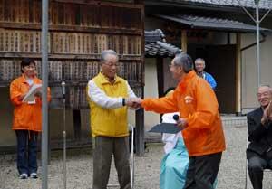 黄色のベストの男性とオレンジ色のジャケットを着た男性が握手している写真