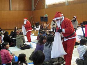 サンタクロースたちが子供たちにプレゼントを渡している写真