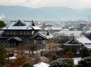 奈良の里山と街並みを背景にうっすら雪を被った城址会館と城ホールの写真