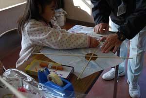 水玉模様のブラウスを着た女の子が凧を作っている写真