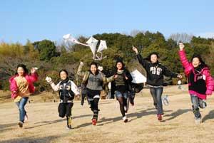女性たちが6人で駆けながら凧をあげている写真