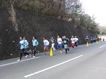 車道に置かれた黄色い三角コーンの内側を走っているマラソン参加者たちの様子の写真