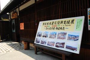 古びた木造の建物の軒下に立てられた「東日本大震災復興支援展」と書かれた大きな横長のパネルの写真