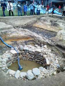 発掘された井戸を遠くから眺めている考古学ファンたちの様子の写真