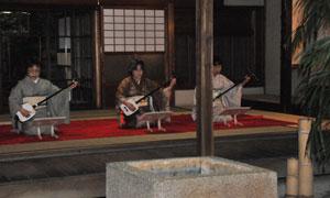 縁側で3人の女性が座って三味線を演奏している様子の写真