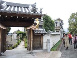 立派な瓦屋根のお寺の入り口付近を人々が歩いている写真